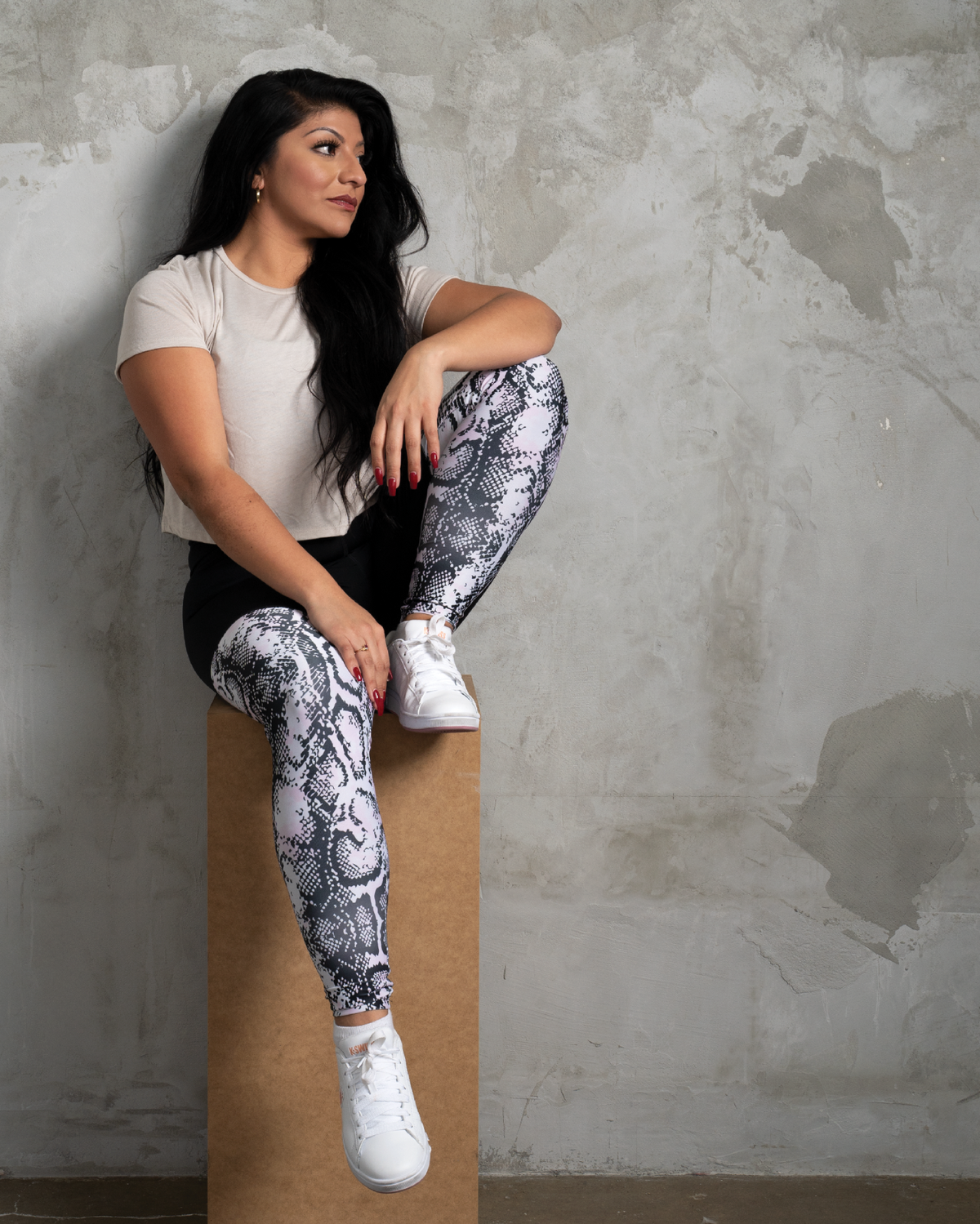 black high waisted leggings in animal pattern and cream crop tee model sitting on a cube in from of concrete wall