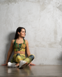 high waisted leggings in green and yellow pattern and crop top model sitting on a floor with a concrete wall behind