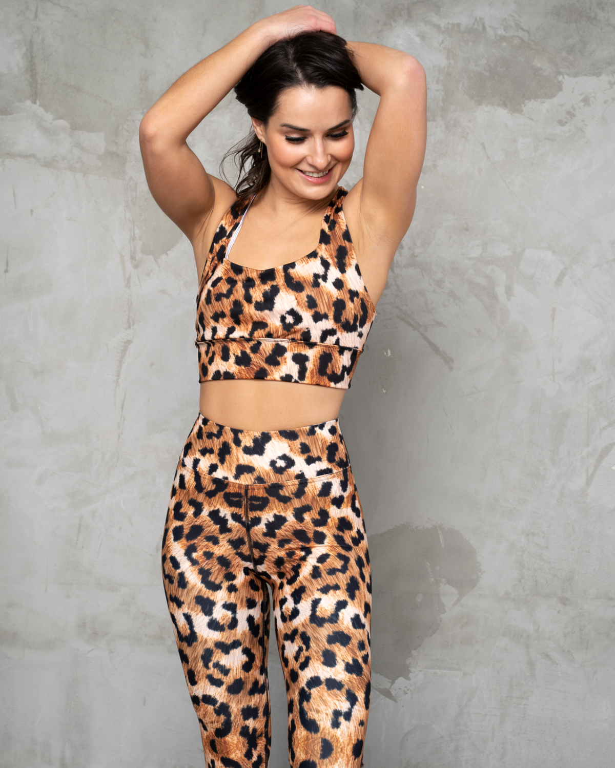 matching activewear set high waisted leggings and longline sports bra crop top in a leopard print on concrete wall